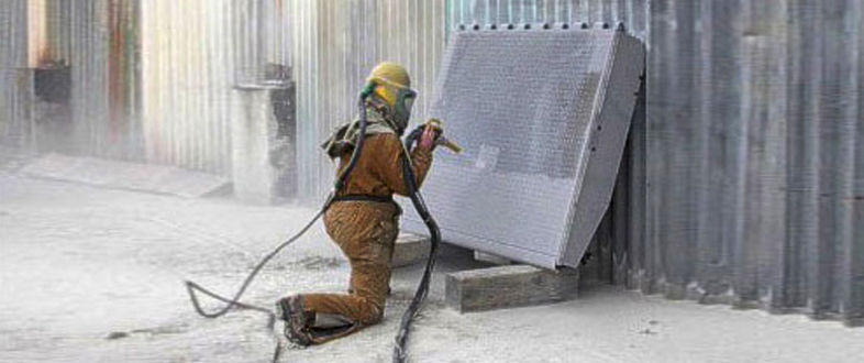 Worker in a blast suit abrasive blasting a steel panel