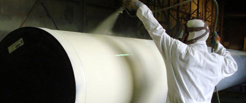 Applicator in protective suit spraying a coating on a large pipe